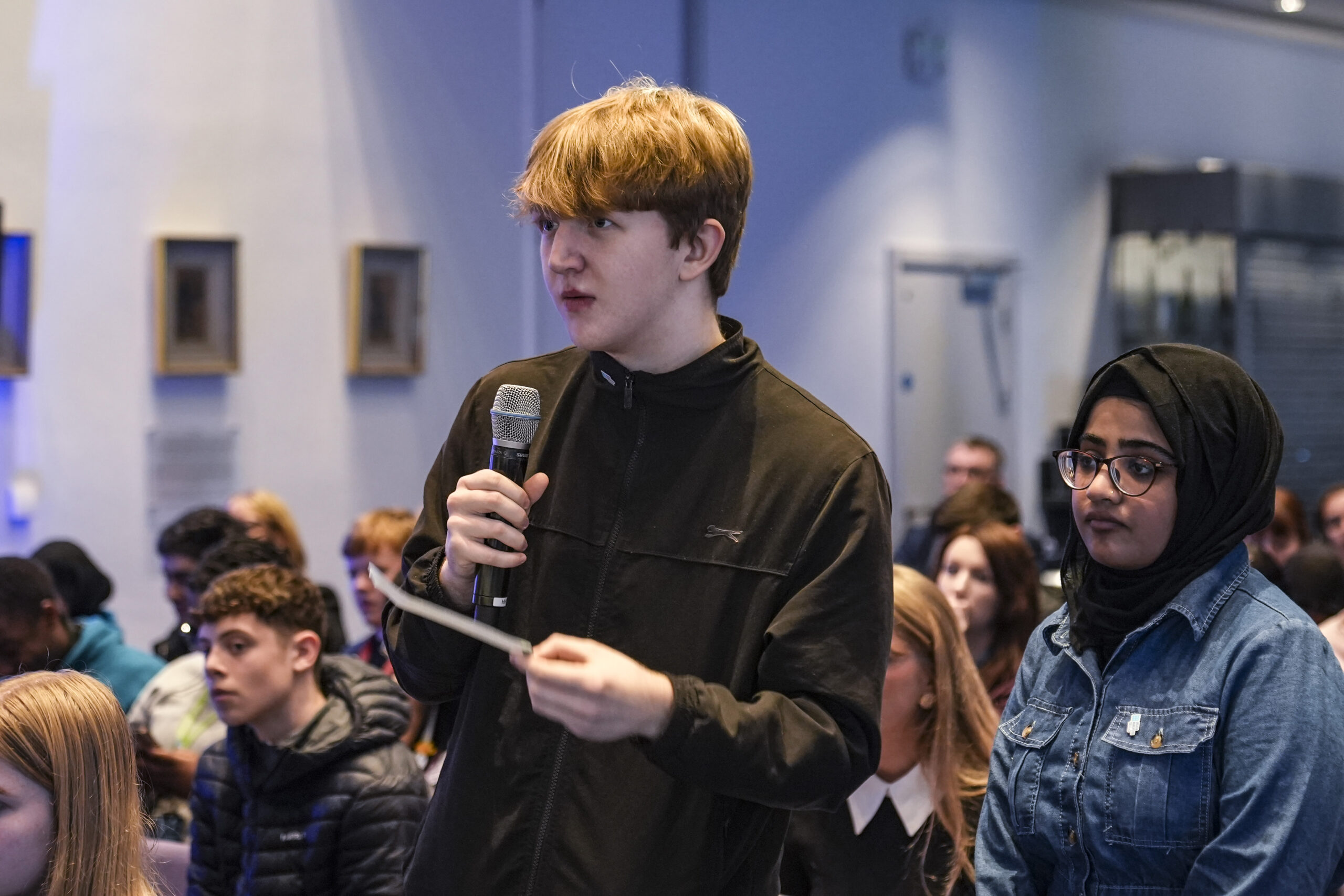 Student stood in a crowd speaking into microphone