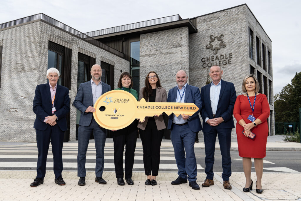 Seven stakeholders standing outside the new Cheadle College campus, holding a large ceremonial key that reads “Cheadle College New Build.”