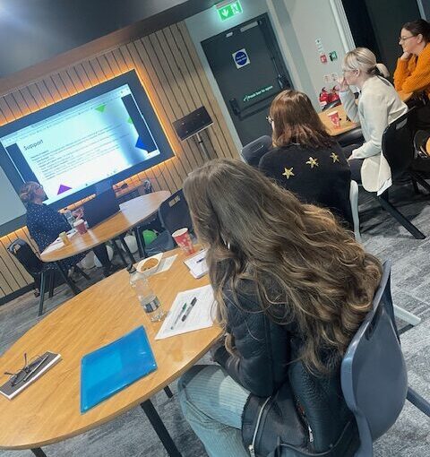 Team induction meeting in a modern conference room with attendees viewing a presentation screen and engaging with materials on the table.