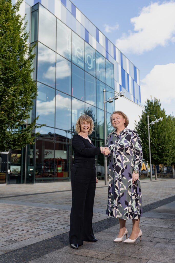 Two women shaking hands while smiling in front of the Light Leisure complex in Stockport