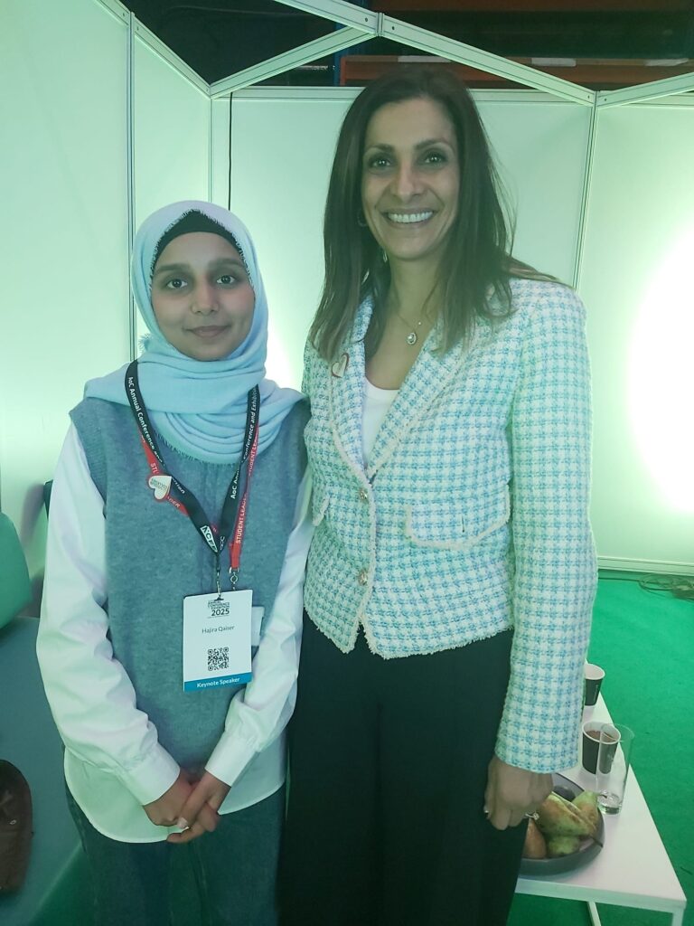 Hajira Qaiser at an education event, wearing a conference badge and standing next to Samin Ali Khan in a networking area.